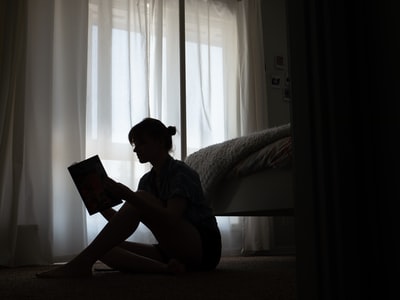 Wearing a blue T-shirt man sat up in bed reading a book
